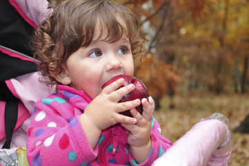 In the forest a little curly-haired girl eats red apple