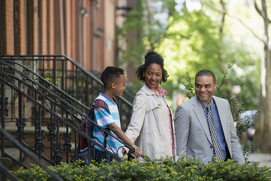 A Family Outdoors In The City. Two Parents And A Young Boy Walking Together. 
