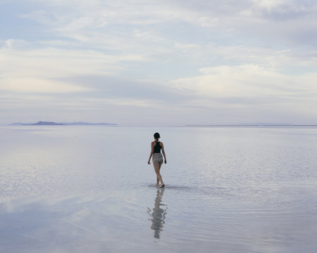 A Woman Standing On The Flooded Bonneville Salt Flats At Dusk. Reflections In The Shallow Water.