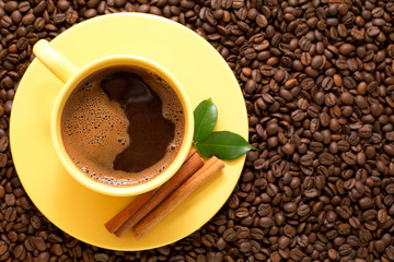 Yellow cup of coffee with cinnamon and green leaves