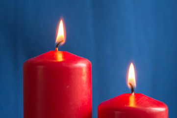 Two burning red candles on a blue background close up