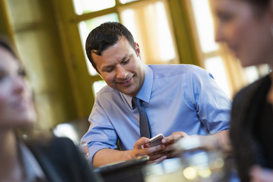 Business People. Three People Around A Cafe Table, One Of Whom Is Checking Their Phone. 