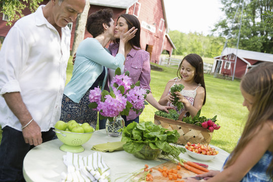 Family Party. A Table Laid With Salads And Fresh Fruits And Vegetables. Parents And Children. A Mother Kissing A Daughter On The Cheek. 