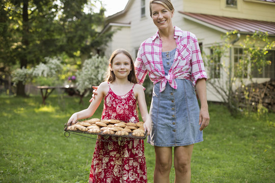 Baking Homemade Cookies. A Young Girl Holding A Tray Of Fresh Baked Cookies, And An Adult Woman Beside Her.