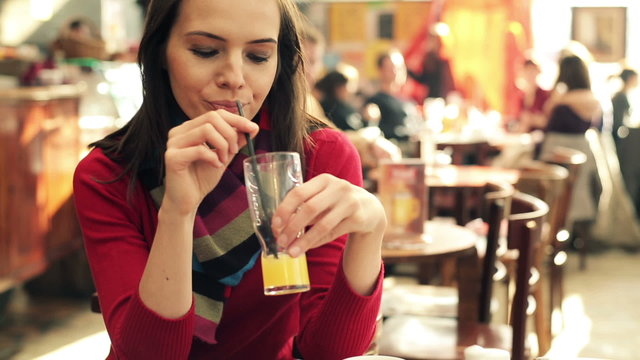 Young beautiful woman drinking juice in crowded cafe