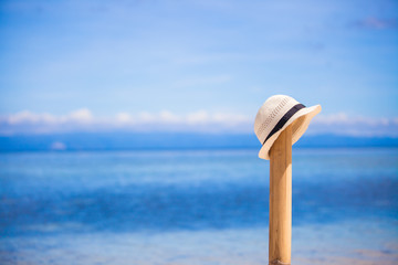 Straw hat at wooden fence on the white sandy beach with an ocean