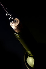 Opening a bottle of wine, on dark background. Green reflection.