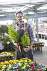 gardener holding two potted plants in a garden center