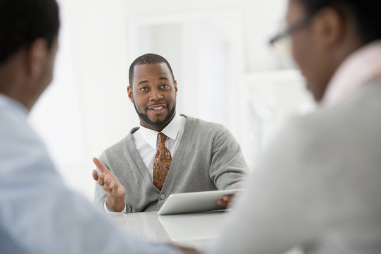Office Interior. Three People Sitting Around A Table At A Business Meeting. 