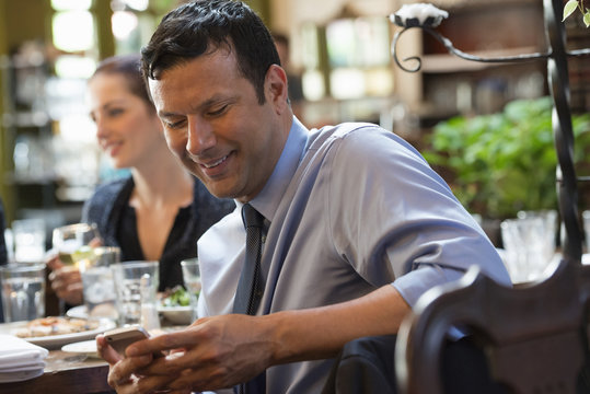 Business People. Three People Around A Cafe Table, One Of Whom Is Checking Their Phone. 