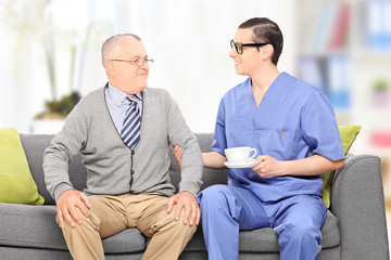 Senior adult and a male nurse sitting on sofa