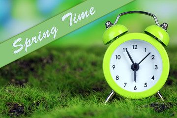 Green alarm clock on grass on natural background