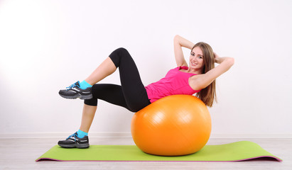 Young beautiful fitness girl exercising with orange ball in gym