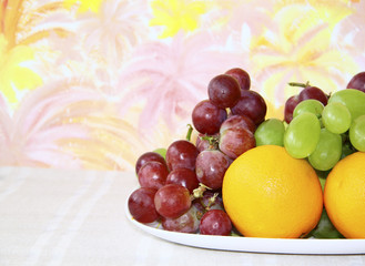 Dish with apples, grapes and oranges on abstract colored backgro