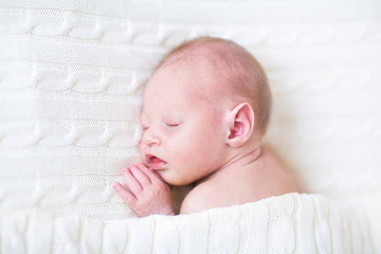Sweet newborn sleeping baby under a knitted blanket