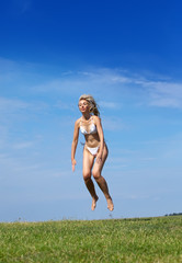 happy woman jumps in summer green field against blue sky..