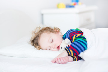 Adorable toddler girl taking a nap in a white bed