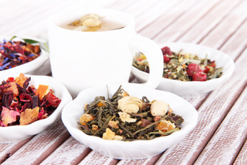 Cup of tea with aromatic dry tea in bowls on wooden background