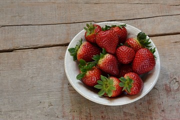 Strawberries in a plate on a wooden table on a wooden table