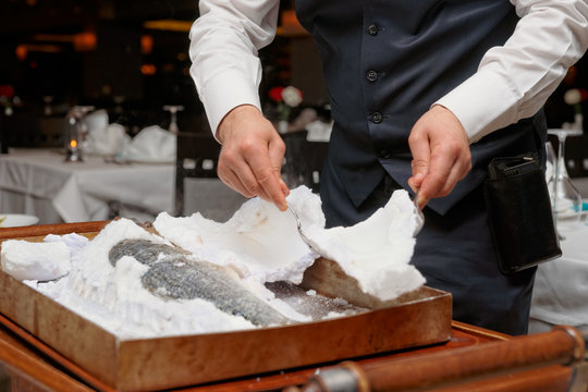 Waiter is carving fish baked in salt crust