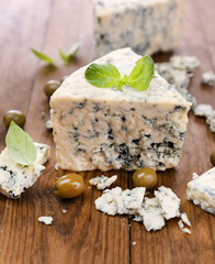 Tasty blue cheese with olives and basil, on wooden table