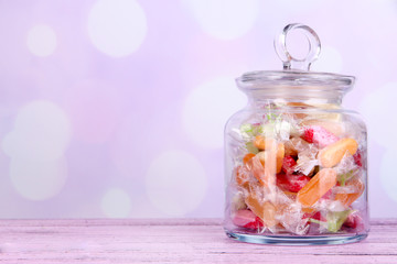 Tasty candies in jar on table on bright background