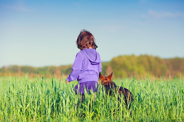 Little girl walking with dog on the field back to camera