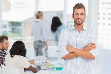 Fototapeta premium Handsome man smiling at camera while his colleagues are working