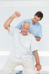 Obraz premium Mhysiotherapist assisting senior man to raise hand