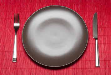 Empty Plate, Fork And Knife On Bamboo Mat