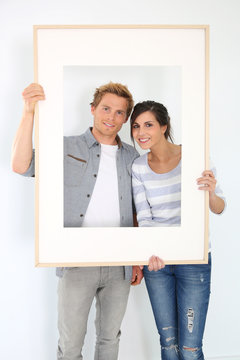 Cheerful young couple holding picture frame to look through