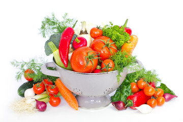 Fresh vegetables in metal colander over white