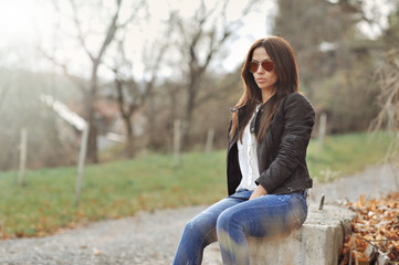 Naklejka na ściany i meble Attractive modern woman sitting in a autumn park