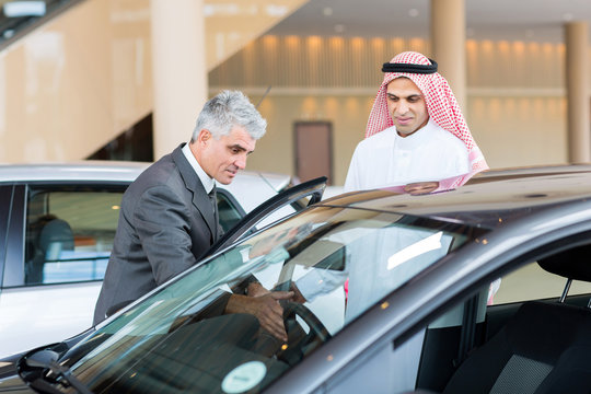 middle aged car dealer showing new car to Arabian buyer