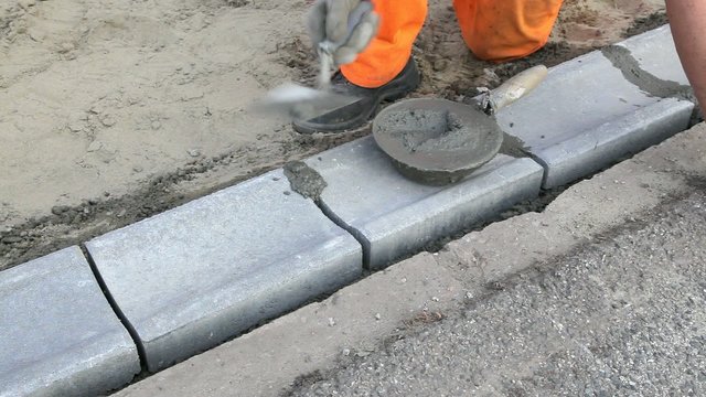 Worker installing curb stone, using trowel and mortar