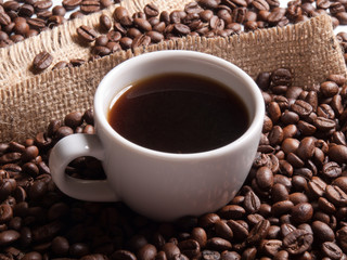 white cup with coffee on burlap background with beans