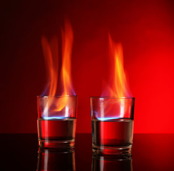 Glasses with burning alcohol on red background