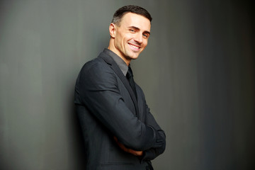 Smiling businessman with arms folded standing on gray background