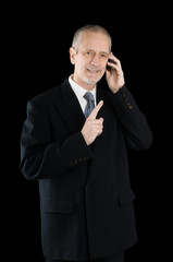 An agreeable businessman wearing a black suit smiling while speaking on mobile phone, on black background