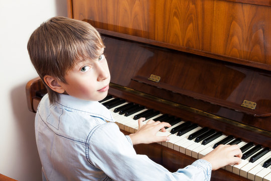 Beatufull little boy playing piano looking into camera