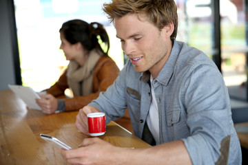 Young man in coffee shop wonnected on smartphone