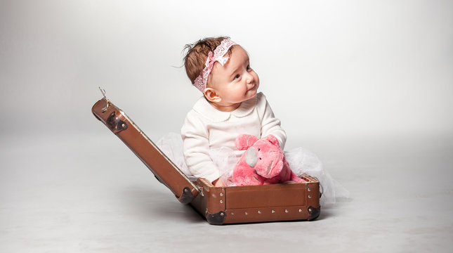 Little smiling girl sitting in suitcase with pink teddy bear
