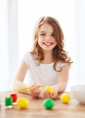 Obraz na płótnie Canvas smiling little girl coloring eggs for easter