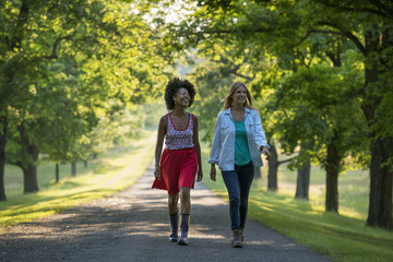 Two women walking down a path lined with trees.