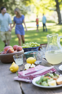 A Summer Buffet Of Fruits And Vegetables, Laid Out On A Table. People In The Background.