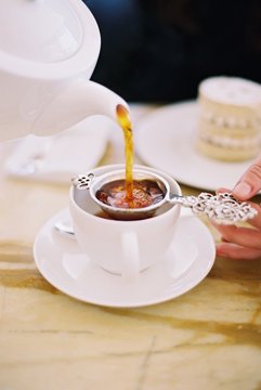 A person pouring a cup of tea, using a strainer. White china. Elegant afternoon tea.