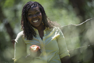 A smiling girl holding a half eaten apple. Sitting on a cart seat. 