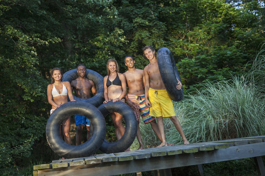 A row of five young people with swim floats on the jetty by a natural pool. 