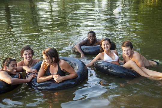 A group of young people, boys and girls, swimming and floating using swim floats and inflated tyres. 