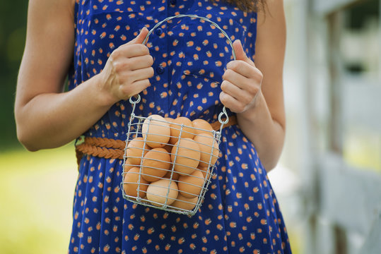 A woman holding a basket of hen's eggs gathered from the chickens on a farm.